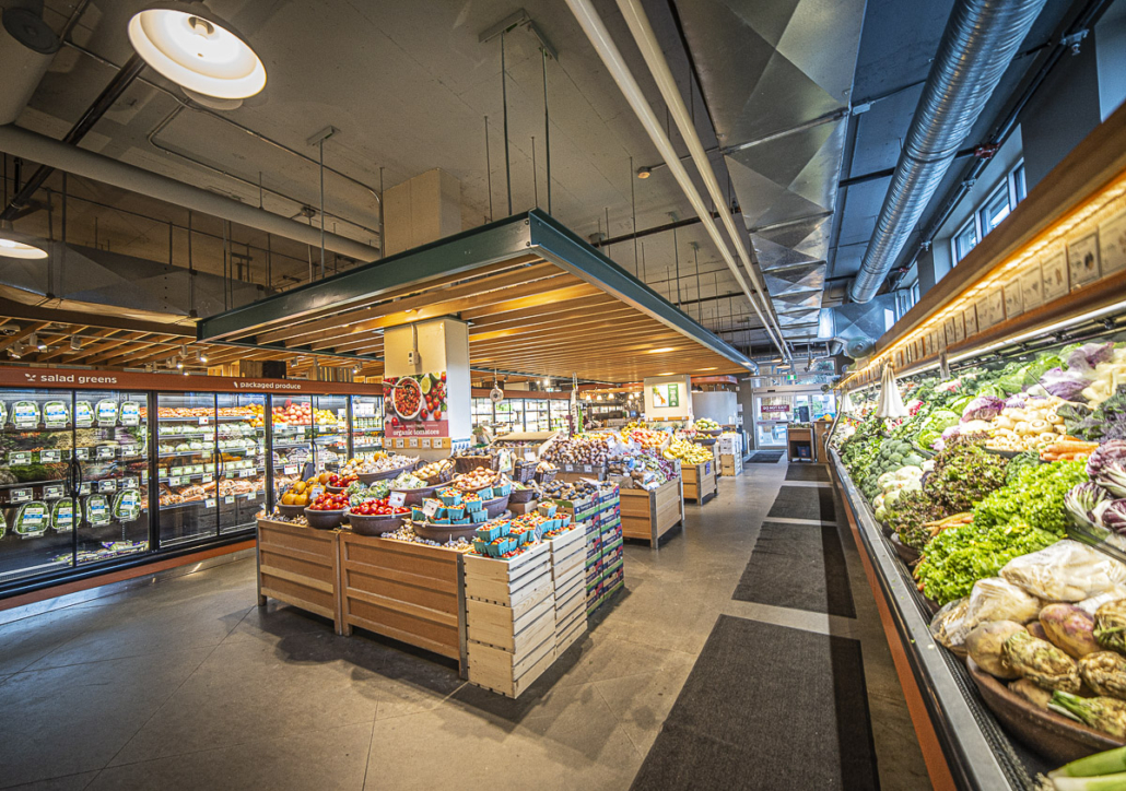 Wooden produce bins piled with fresh fruit and vegetables under exposed ductwork at the Kootenay Coop in Nelson, BC.