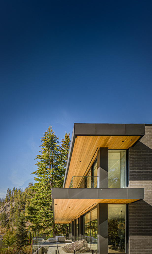 Angled cedar-lined balconies and dark brick cladding on a modern Nelson, BC home against a clear sky.